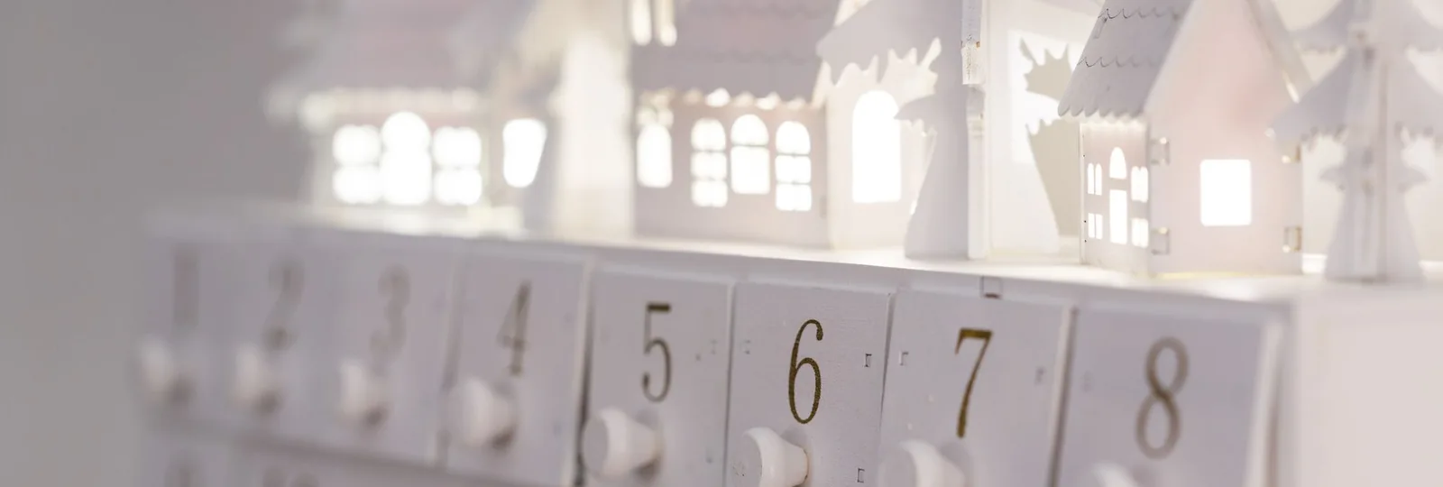 Weißer Adventskalender mit nummerierten Schubladen und beleuchteten Häuschen darauf