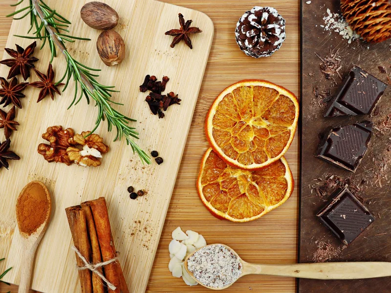 Holzbrett mit Sternanis, Zimt, Nüssen, getrockneten Orangenscheiben und dunkler Schokolade