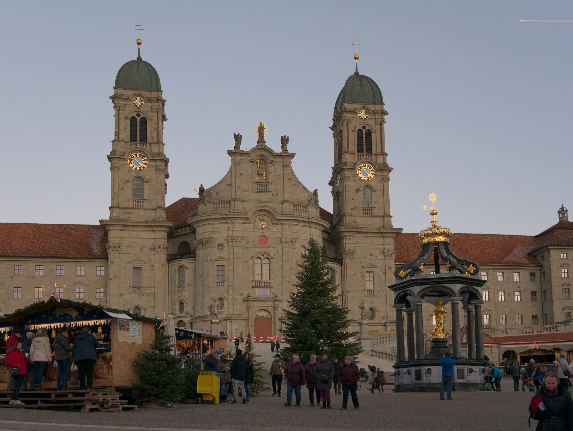 Weihnachtsmarktstände auf dem Klosterplatz in Einsiedeln in der Dämmerung vor der Fassade des Klosters