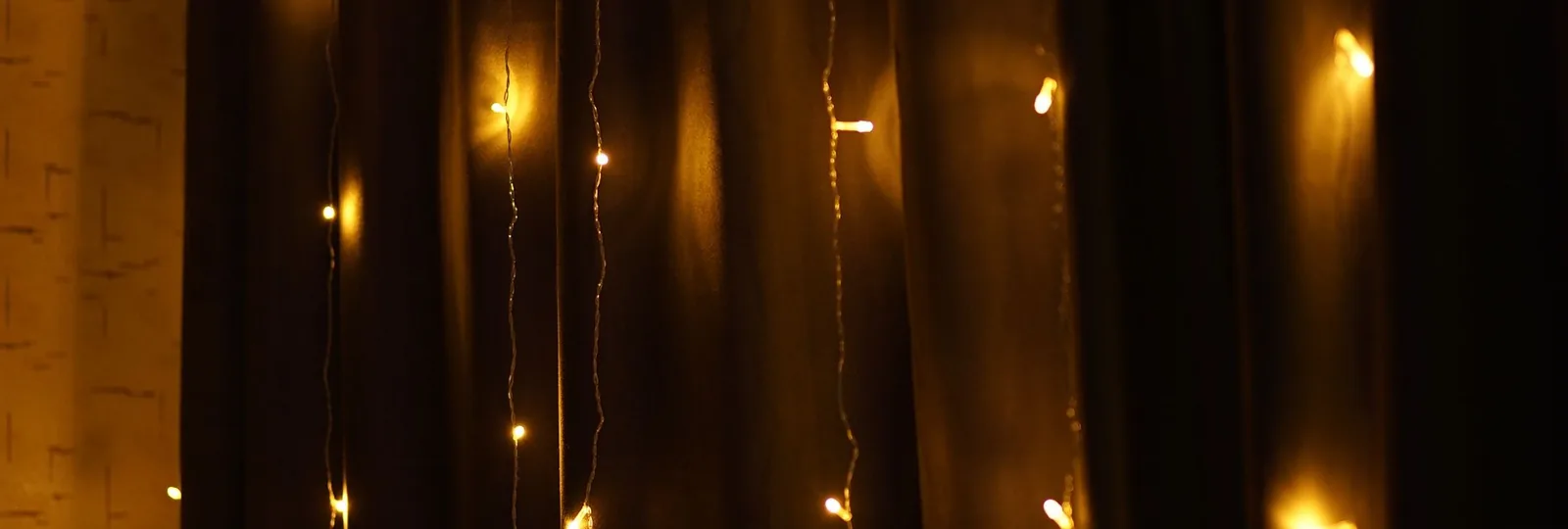 Warm leuchtende Lichterkette mit feinen Drähten vor einem dunklen Vorhang