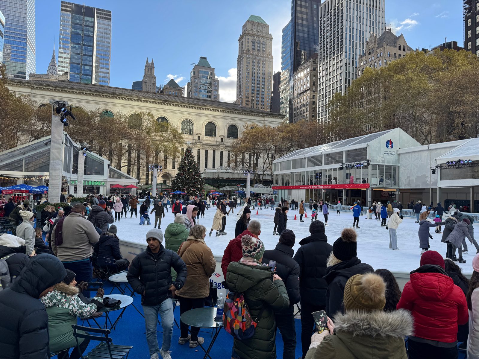 Eisbahn und Marktpavillons des Winter Village im Bryant Park in New York, dahinter die Hochhäuser von Midtown Manhattan