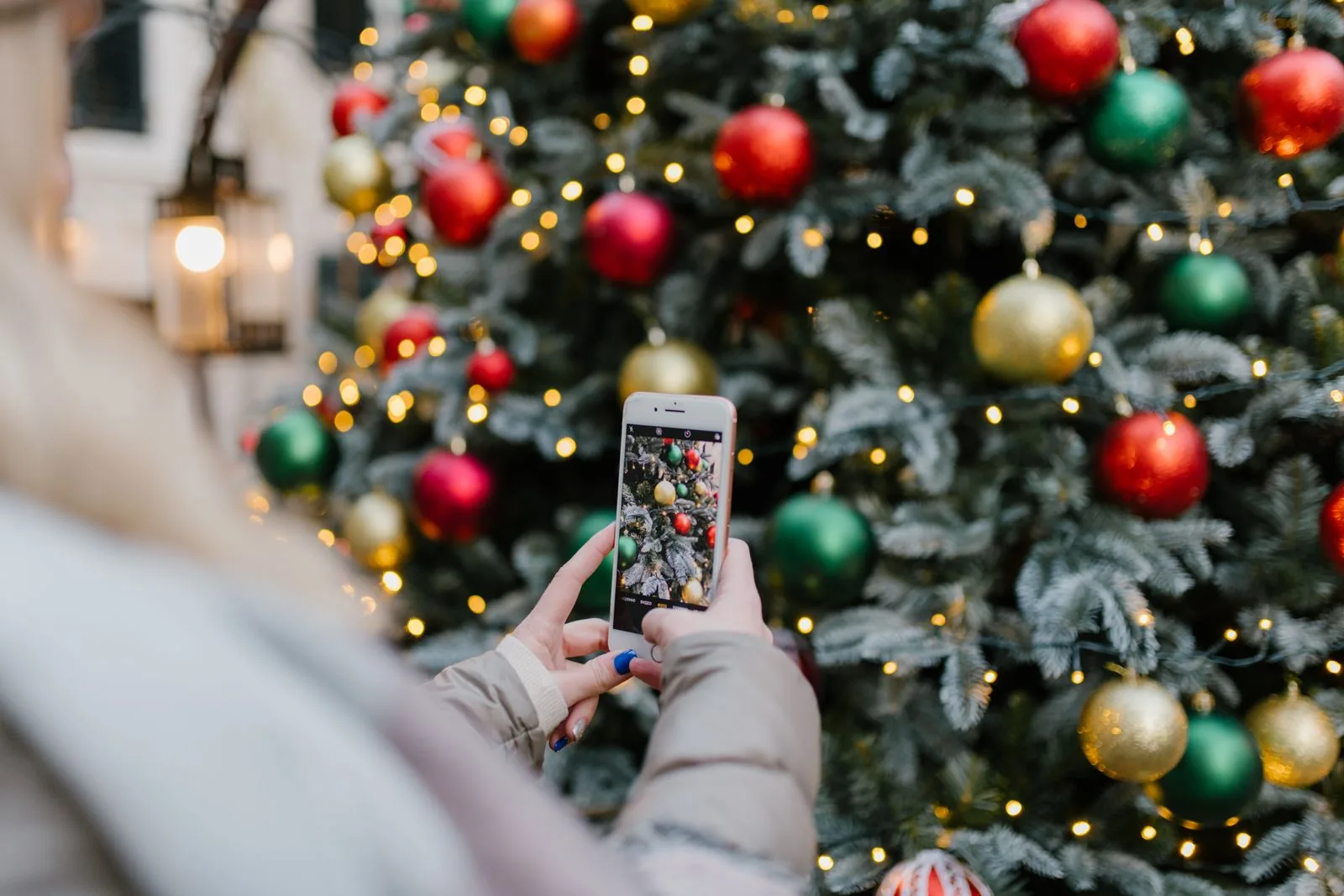Hände halten ein Smartphone und fotografieren einen geschmückten Weihnachtsbaum mit warmen Lichtern
